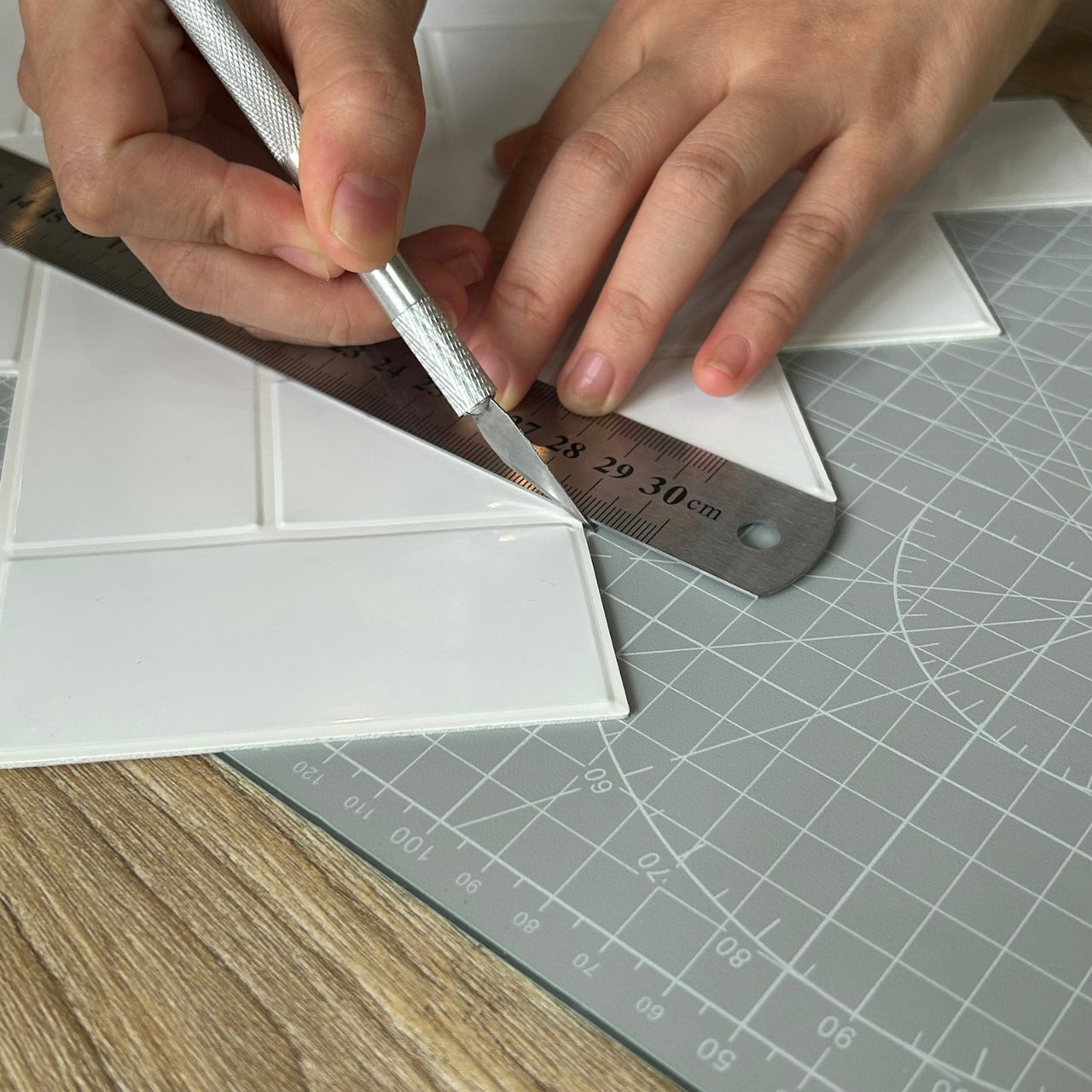 Craft knife following edge of metal edge ruler to cut peel and stick wall tiles